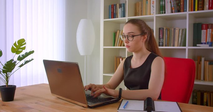 Closeup portrait of young pretty redhead businesswoman in glasses using laptop and getting surprised in office indoors