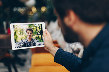Young man using a tablet to chat with his friend. Long distance video call concept.