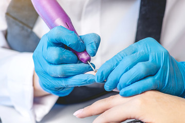 Woman manicure master makes a hardware manicure cutter removing the cuticle in the salon. Beauty...