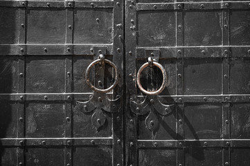 Ancient church door. Close-up of an old black metal door with rings and rivets.