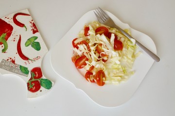 Tasty tomato cabbage salad in the white plate with fork.
