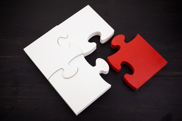 Three onnected jigsaw puzzle pieces and one red on dark wooden background. Finding the right solutions in teamwork.