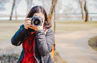 Beautiful young girl with SLR camera taking photo in park outdoors looking at camera. Photographer profession.