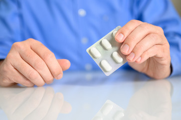 Mann mit Medikamenten in der Hand am Schreibtisch