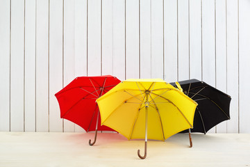 Three umbrellas on floor near white wooden wall with space for design