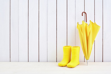 A pair of yellow rain boots and a umbrella on white wooden background