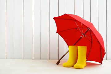 A pair of yellow rain boots and a umbrella on white wooden background © vetre