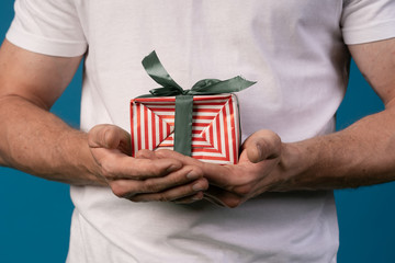 happy handsome man giving a christmas gift, on blue background. red striped box with a green ribbon.