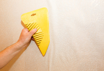Man is using scraper to install wallpaper. Levelling of the wall. Maintenance repair works renovation in the flat. Restoration indoors.