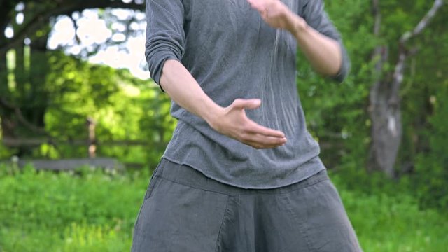 An average plan a young man in Indian clothes and pants Aladdin practices qigong while doing exercises while working with qi energy outdoors in summer next to an old hut