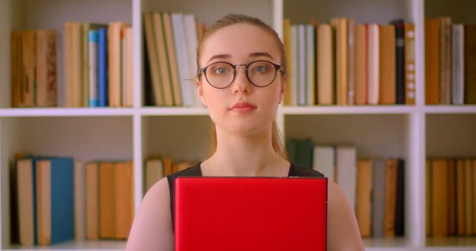 Closeup portrait of young successful redhead businesswoman in glasses holding laptop in office indoors