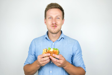 young smiling man biting cheeseburger from fast food restaurant standing with salad leaf in his mouth on isolated white background