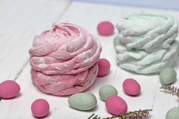 Pink and mint marshmallows in icing sugar. Lies on white painted boards. Nearby, stones of different colors are scattered for decoration. Heather branches are also visible.