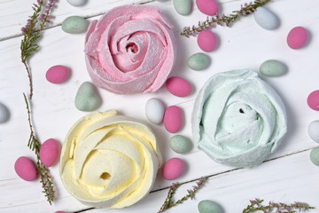 Pink and mint marshmallows in the form of a flower in icing sugar.  Different color. Lies on white painted boards. Nearby, stones of different colors are scattered for decoration. Heather branches