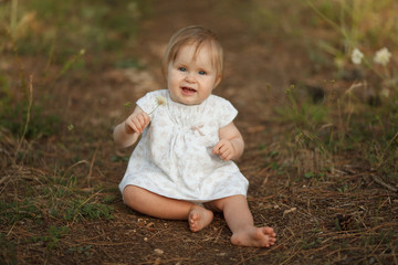 Cute happy little baby girl with flower in nature in the forest sitting and smiling. Looking at the camera. The concept is tenderness, naivety, simplicity, family, motherhood.