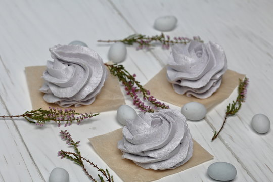 Freshly made lavender marshmallows on white painted boards. Nearby, stones are scattered for decoration. Heather branches are also visible.