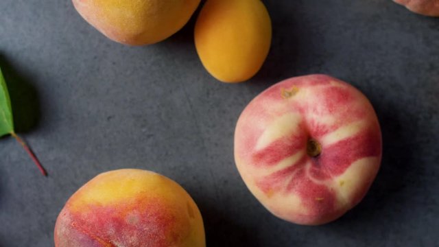 Nice yummy fresh apricots and peaches with green tree leaves on dark texture surface. Top view. Summer fruits. 4k.