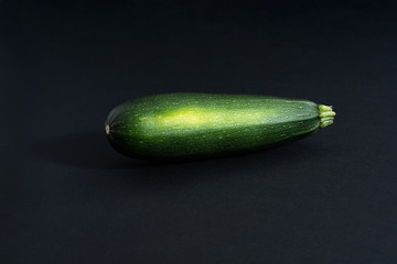 on a black background one raw green whole zucchini, close-up top view, copy space, horizontal frame