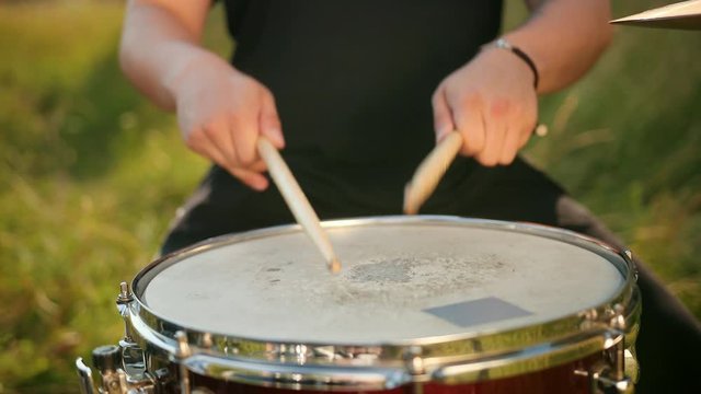 professional musician drummer dressed in black clothes, vigorously playing on the drum set, on the street. on a Sunny day, around the tall green grass, slow motion, close-up