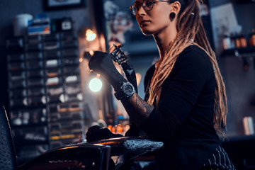 Pretty expirienced tattoo artist in glasses is tuning her new tattoo machine before tattooing...