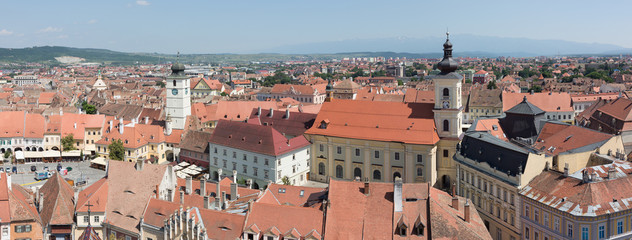 Naklejka na ściany i meble SIBIU, ROMANIA - June 27, 2019: Panorama view of Sibiu Old Town. On the right the Roman Catholic Church, on the left the market square. Sibiu was European Capital of Culture in 2007. Aerial, rooftops.