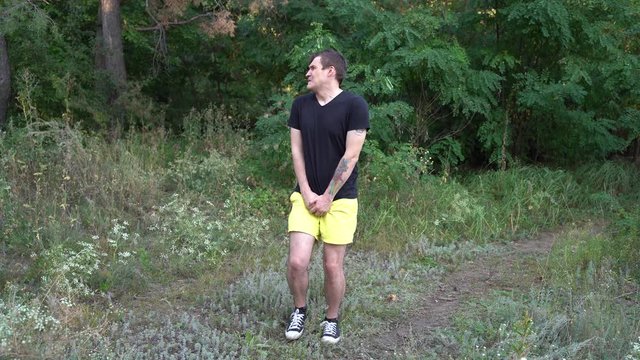 A handsome young man is suffering from the urge to pee in the forest.
