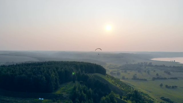 Foggy landscape with green trees and a paraglider flying above it