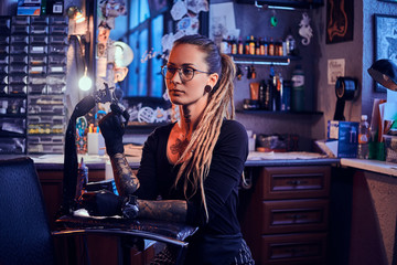 Pretty expirienced tattoo artist in glasses is tuning her new tattoo machine before tattooing...