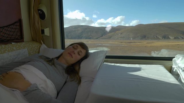 CLOSE UP: Young woman napping in the soft bed of overnight train crossing the vast Tibetan plains. Tired female traveler sleeps in her first class cabin during a train journey across stunning Himalaya