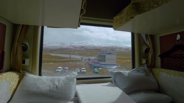 CLOSE UP: Sleeper train window provides a stunning vista of the rugged Himalayan nature. Two comfortable beds remain empty in a private sleeping cabin of an overnight train crossing picturesque Tibet.