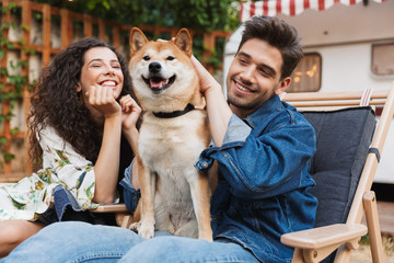 Happy positive loving couple man and woman near trailer mobile home hugging their dog.