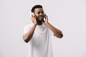 smiling african american man listening music and touching headphones isolated on white