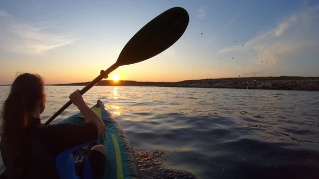 Woman padling her kayak at sea towards the sunset
