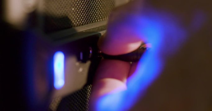 A blue light from a computer that indicates it is on reflects off the hand of a Caucasian male that is unplugging a headphone jack from the designated socket. Macro Shot, Extreme shallow DOF