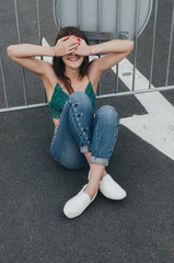 Pretty brunette girl sitting on the road and closed her eyes with hands waiting for surprise