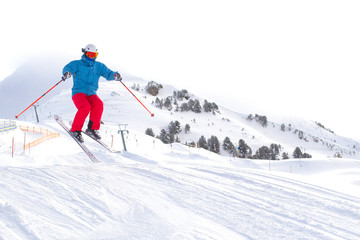 Skier man with orange ski glasses in white helmet make release jump on ski slope on top in Alps mountains. On the background of mountains. Close up view.