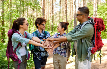 travel, tourism, hike and friendship concept - group of friends with backpacks stacking hands in forest