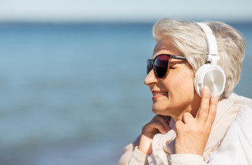 technology, old people and leisure concept - senior woman in headphones and sunglasses listening to music on summer beach in estonia