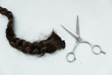 Hairdresser's scissors with cut pigtail of brown hair on gray wooden background. Copy space. Top view. Flat lay