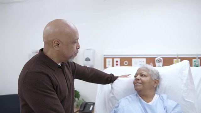 Elderly female hospital patient in a patient gown shares a kiss with husband