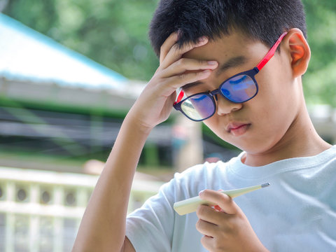 Asia Boy Measuring Temperature Of Himself Ill. Sick Child With High Fever And Holding Thermometer.