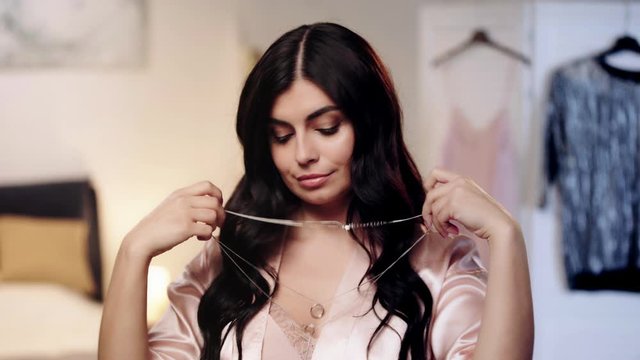 brunette woman in pink satin robe choosing necklace