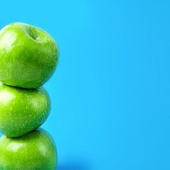 Stacked ripe green organic apples on blue background. Vegan food weight loss detox vitamins plant based diet concept. Trendy minimalist poster in square format for social media.