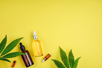 Bottles with CBD oil, a dropper, and leaf marijuana on yellow background. Concept beauty care with...