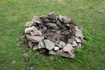 Obraz premium Fireplace and campfire ring - stones and ashes. Green grass around camp fire. 