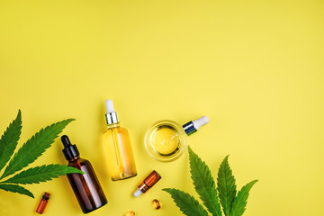Bottles with CBD oil, a dropper, and leaf cannabis on a yellow background. Concept beauty care with...
