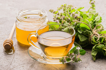Cup of tea drink with fresh leaves of mint melissa and honey gray background. Healing herbal drink....