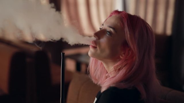 Sexy unconventional woman with pink hair smoking hookah in the club