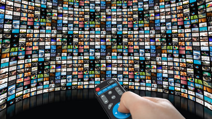 Image of large screen with many channels, hands of man with remote control.