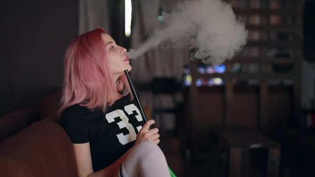 Sexy unconventional woman with pink hair smoking hookah in the club